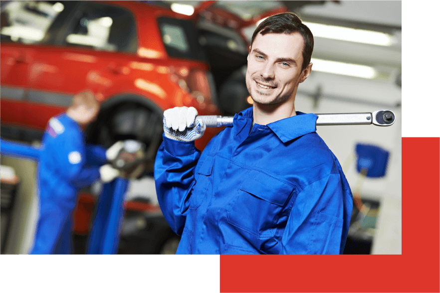 A close-up of a smiling auto mechanic wearing a blue suit and  white gloves and carrying a tool on his shoulder.
