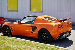 A side view of an orange Lotus car parked on a driveway.