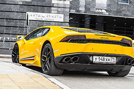 A rear view of a yellow Lamborghini on a side walk.