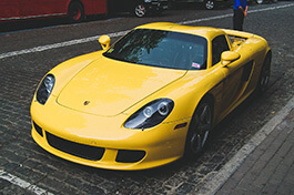A full shot of a yellow porsche car on the side of a road.